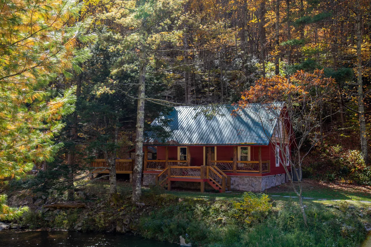 This exterior shot showcases a rustic 1930s cabin nestled among trees, with a calm body of water nearby. The scene is peaceful and inviting, highlighting both the historic charm of the lodge and the natural beauty of its setting—suggesting opportunities for porch relaxation and sunset views over the lake.