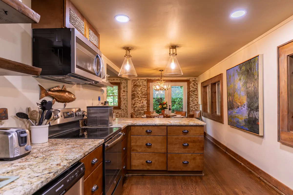 A warmly lit kitchen with granite countertops, wooden cabinets, hanging light fixtures, and a piece of artwork on the wall. The open layout encourages both cooking and socializing, while the modern appliances blend seamlessly with the rustic, heritage-inspired materials.