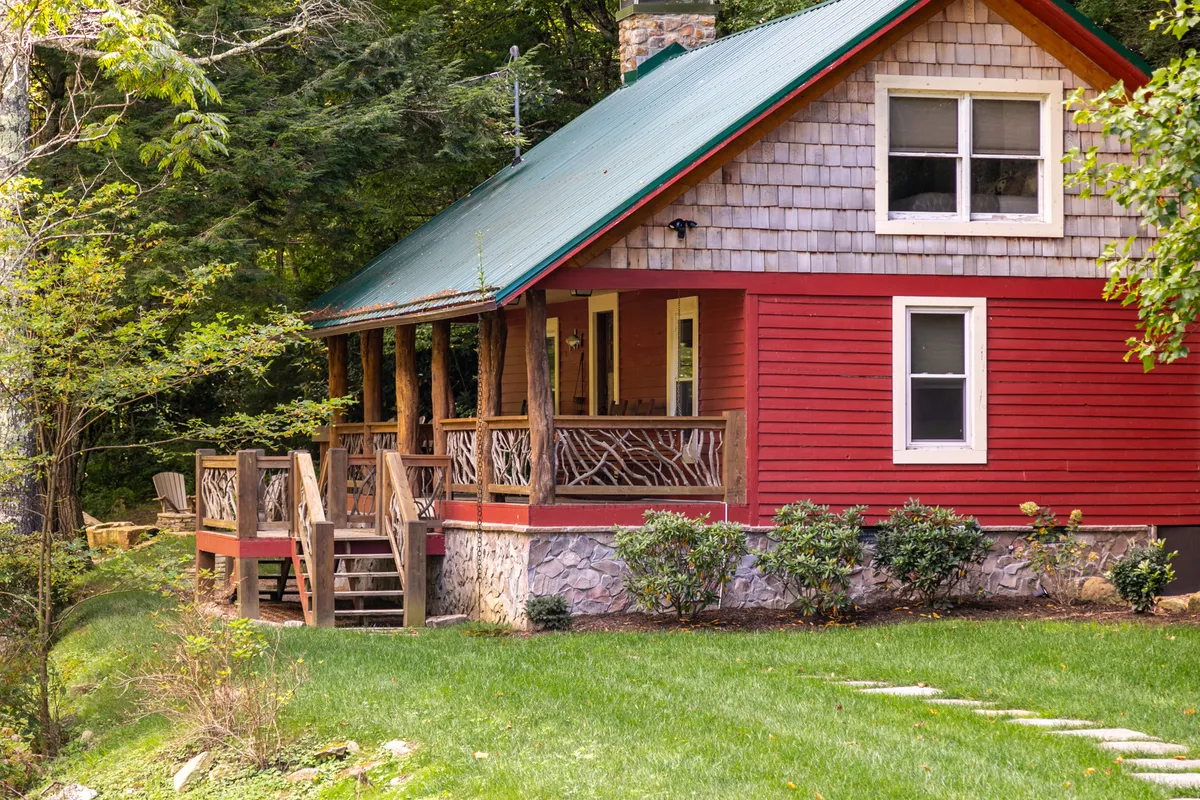 This exterior image showcases a welcoming red cabin with a wooden porch, a stone foundation, and a surrounding natural landscape. The porch provides a clear visual invitation for relaxing, gathering, and enjoying the outdoors, all while emphasizing the sense of community that resort-style amenities offer.