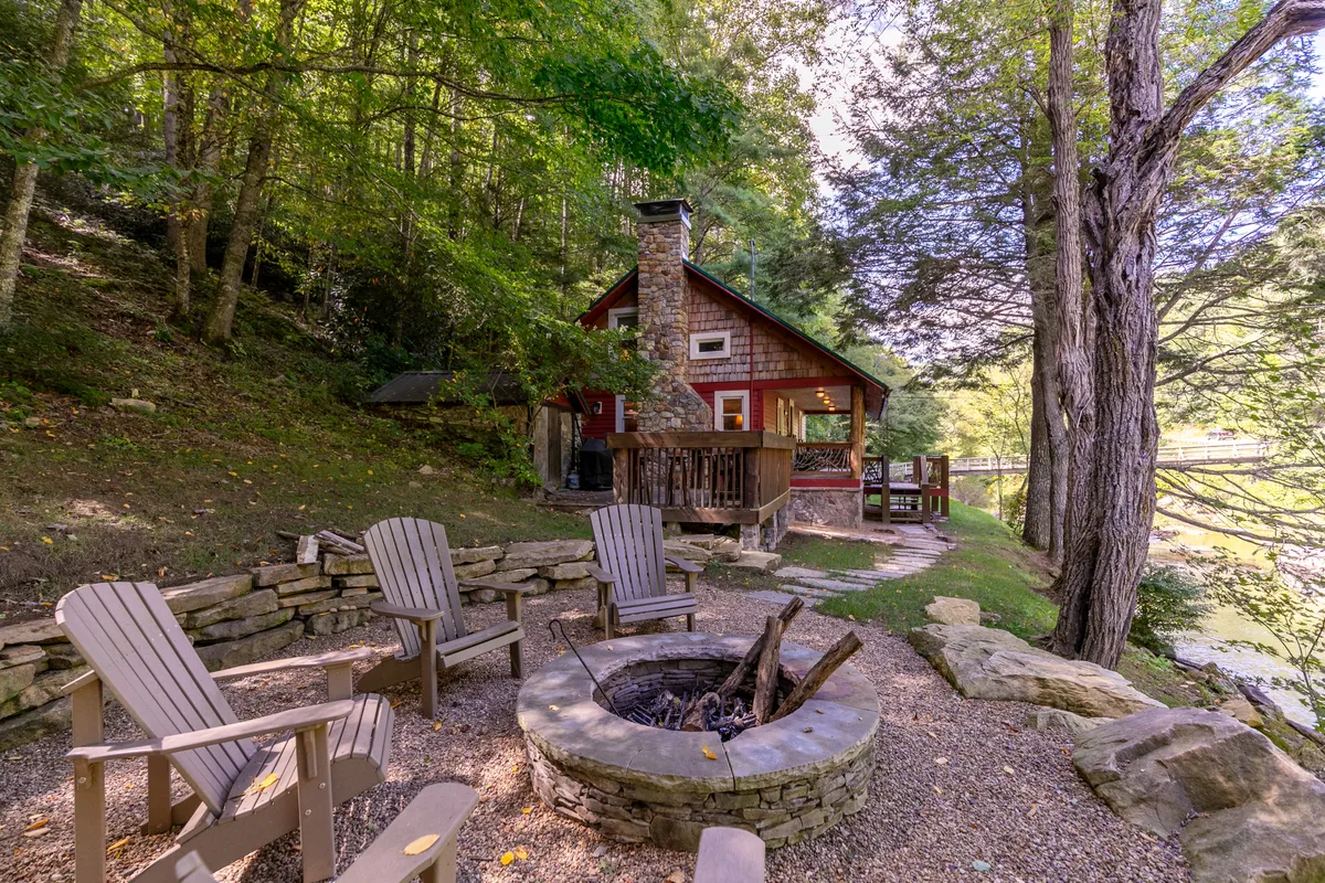 A cozy outdoor area with a fire pit surrounded by Adirondack chairs, nestled among trees and facing a charming cabin. The mood is intimate and tranquil, perfect for evening gatherings, stargazing, or making s'mores by the fire. The cabin and natural surroundings reinforce the connection between luxury accommodations and the beauty of nature.