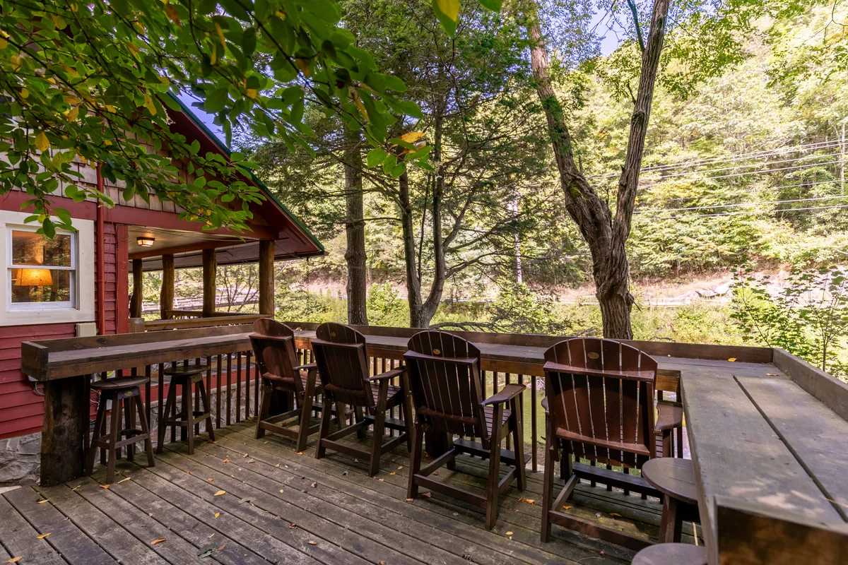 A peaceful wooden deck overlooking the water, framed by Adirondack chairs and surrounded by lush trees. The view invites guests to relax, socialize, and enjoy coffee or a glass of wine while taking in sunset vistas and the tranquil ambiance of the outdoors.