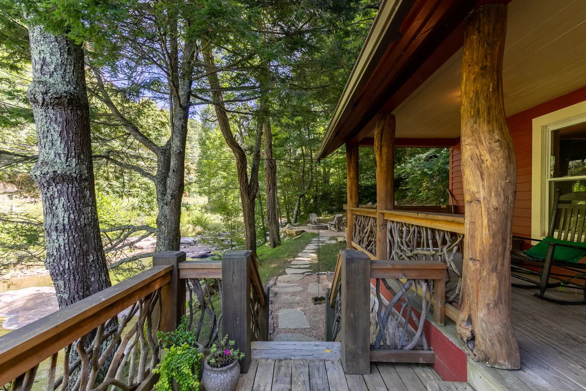An exterior view of the lodge’s porch area, supported by wooden pillars and framed by a rock pathway and greenery. The porch is inviting, hinting at sunset views, nature walks, and the ease of moving between indoor and outdoor spaces.