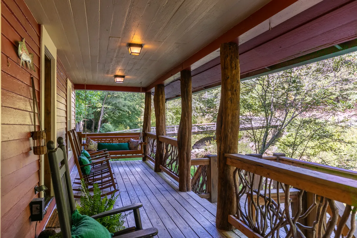 A welcoming porch scene with wooden rocking chairs and railings, lush greenery, and a bridge in the distance. This spot offers guests a place to relax, watch wildlife, stargaze, or host a summer barbecue, showcasing the lodge's inviting exterior spaces.