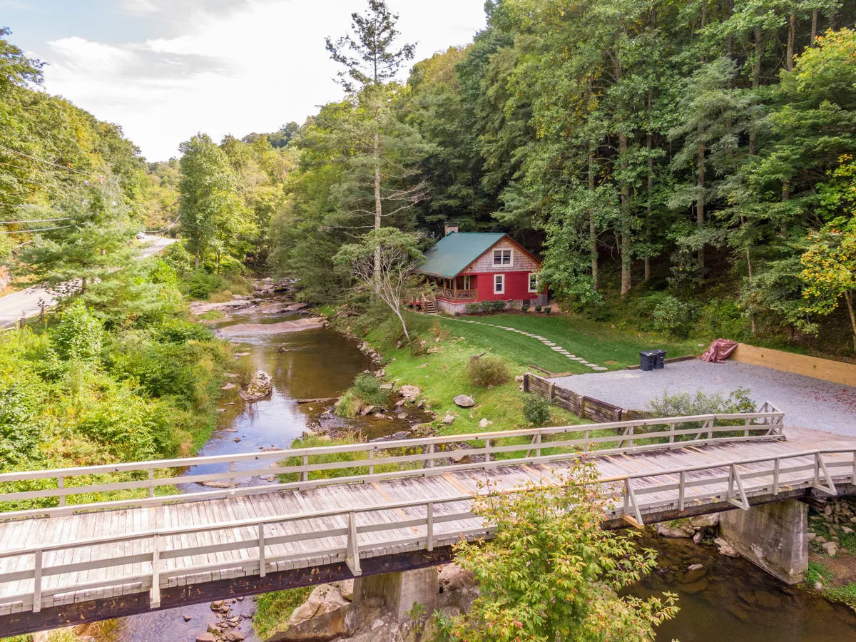 An exterior view of the red cabin with a wooden bridge over a stream, surrounded by trees. The area is ideal for fishing, hiking, picnicking, and enjoying the peaceful natural setting, highlighting the outdoor adventure and relaxation opportunities at Elk River Fish Lodge.