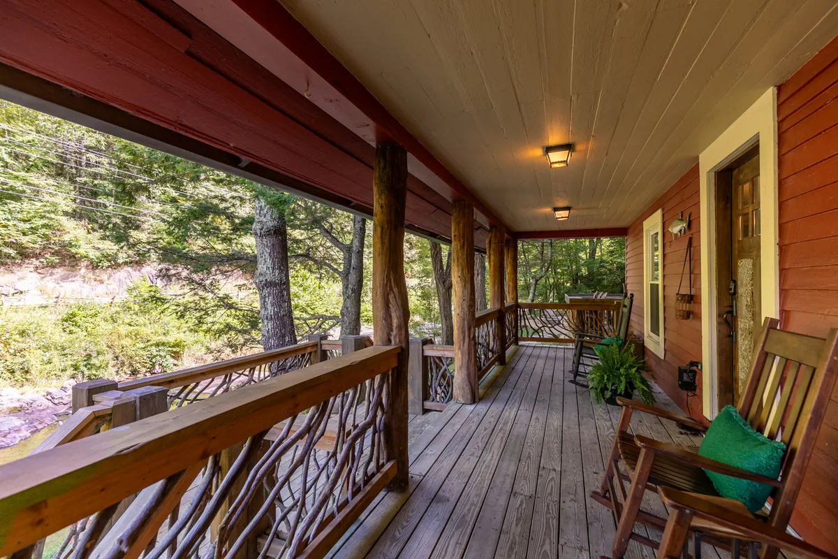 The image focuses on a tranquil exterior with rocking chairs on a wooden porch, lush greenery all around, and a welcoming front door. This scene emphasizes relaxation, social connection, and the enjoyment of the peaceful environment just outside the home.